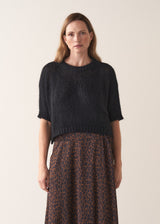 Woman wearing a black sparkle knit short sleeve sweater and a leopard print skirt on a plain background