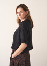 Woman side on wearing a sleeveless sparkle knit with leopard print skirt.