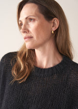 Woman wearing a black sparkle knit short sleeve sweater and a leopard print skirt on a plain background