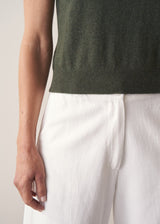 Woman wearing dark green fine knit sweater with removable heart brooch with white barrel leg jeans