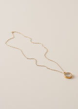 A long, delicate gold chain necklace with a circular pendant featuring grey crystals on a neutral beige background