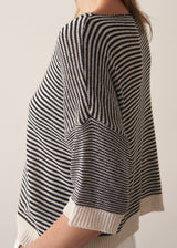 Woman wearing navy and white stripe light knitted sweater and white barrel leg jeans