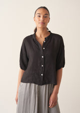 Woman wearing a black linen top and striped, cropped satin trousers against plain background