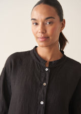 Woman wearing a black linen top and striped, cropped satin trousers against plain background