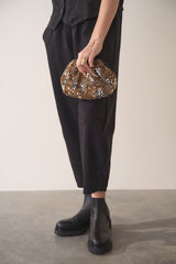 Woman holding a gold sequin embellished clutch bag, wearing black trousers and Chelsea boots.
