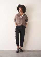 Woman wearing an oatmeal sweater with white shirt and black slim fit drawstring trousers against a neutral background