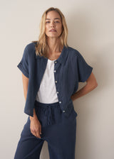 Woman wearing a navy blue short-sleeve linen shirt open over a white tee with linen wide-leg trousers