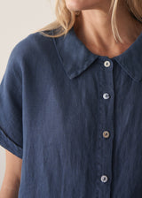 Woman wearing a navy blue short-sleeve linen shirt fastened with mother-of-pearl buttons