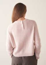 A woman wearing a pale pink boxy sweater with dark check barrel leg trousers