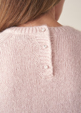 A woman wearing a pale pink boxy sweater with dark check barrel leg trousers