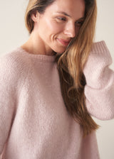 A woman wearing a pale pink boxy sweater with dark check barrel leg trousers