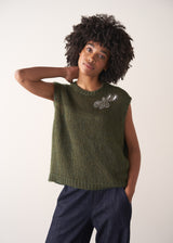 Person wearing a green knitted sleeveless sweater with a silver beaded embellishment