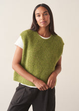 A woman wearing a bright green sleeveless sweater with a white t-shirt and charcoal checked barrel leg trousers
