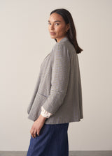 A woman models a blue-green checked cotton jacket over a white shirt, paired with blue jeans, set against a beige background