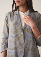 A woman models a blue-green checked cotton jacket over a white shirt, set against a beige background