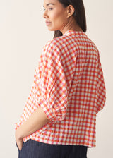 Woman wearing pink and orange gingham shirt with blue jeans