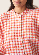 Woman wearing pink and orange gingham shirt with blue jeans