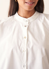 A woman wearing a white-button down cotton shirt with three-quarter puff sleeves and a relaxed fit, with blue denim jeans.