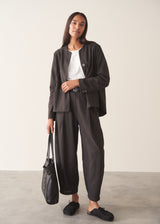 Woman wearing black check barrel leg trousers with a matching check jacket, white t-shirt and leather tote bag.