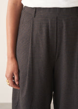 Woman wearing black check barrel leg trousers with a matching check jacket, white t-shirt and leather tote bag.