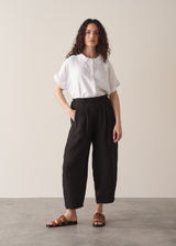Woman wearing white linen shirt and black ankle length linen barrel leg trousers