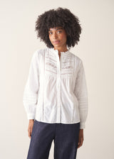 A woman wearing a white, embroidered detail shirt with blue denim jeans.