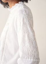 A woman wearing a white, embroidered detail shirt with blue denim jeans.