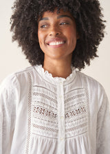 A woman wearing a white, embroidered detail shirt with blue denim jeans.