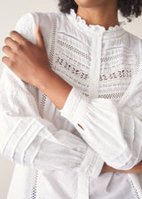 A woman wearing a white, embroidered detail shirt with blue denim jeans.