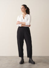 A woman wearing a white top and black barrel leg trousers with chunky boots against a plain background