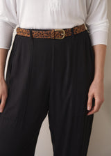 Close up of woman wearing a white top and black barrel leg trousers against a plain background