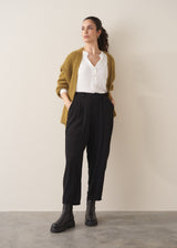 A woman wearing a white top and black barrel leg trousers with green cardigan and chunky boots against a plain background