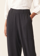 A woman wearing a white v-neck top and black slimtapered trousers.