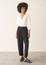 A woman wearing a white v-neck top and black slimtapered trousers.