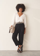 A woman wearing a white v-neck top and black slimtapered trousers.