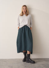 Woman wearing dark green linen cocoon skirt with grey jumper