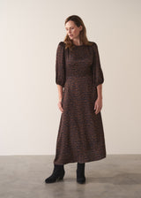 Woman in a round neck leopard print satin midi dress with suede boots, against a plain background