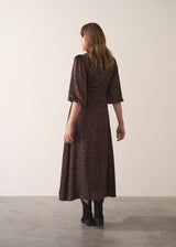 Woman in a leopard print satin midi dress standing against a plain background