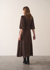 Woman in a leopard print satin midi dress standing against a plain background