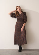 Woman in a round neck leopard print satin midi dress and suede boots against a plain background