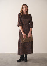 Woman in a round neck leopard print satin midi dress holding a brown clutch against a plain background