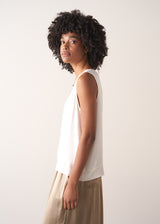 Woman wearing a white sleeveless top against a plain background