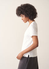 A woman wearing a white short-sleeve v-neck t-shirt and dark grey wide-leg trousers.