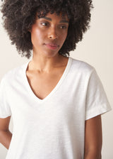 A woman wearing a white short-sleeve v-neck t-shirt and dark grey wide-leg trousers.