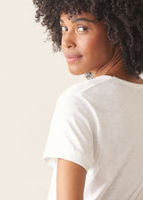 A woman wearing a white short-sleeve v-neck t-shirt and dark grey wide-leg trousers.