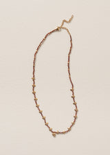 Necklace with plum crystal beads, gold discs, and a hammered heart pendant, on a beige background