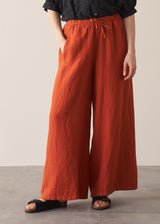 Woman wearing black broderie anglaise top and full length, wide leg red linen trousers