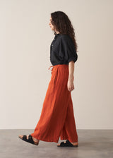 Woman wearing black broderie anglaise top and full length, wide leg red linen trousers