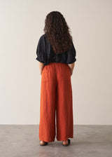 Woman wearing black broderie anglaise top and full length, wide leg red linen trousers