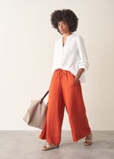 Woman wearing bright red wide leg linen trousers and white v-neck top